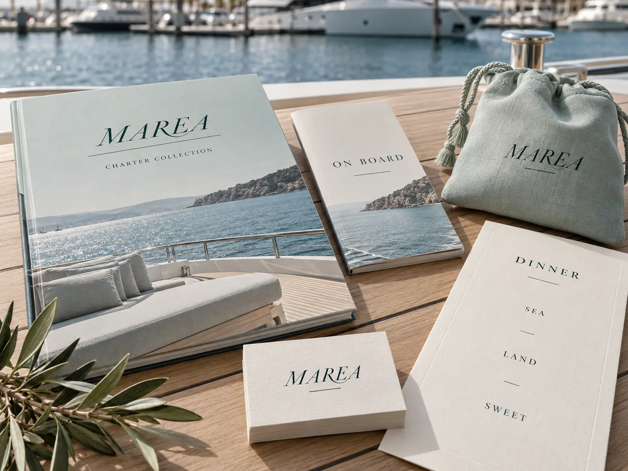 MAREA studio concept: a charter book, on-board guide, dinner menu, cards and a linen pouch on a teak deck